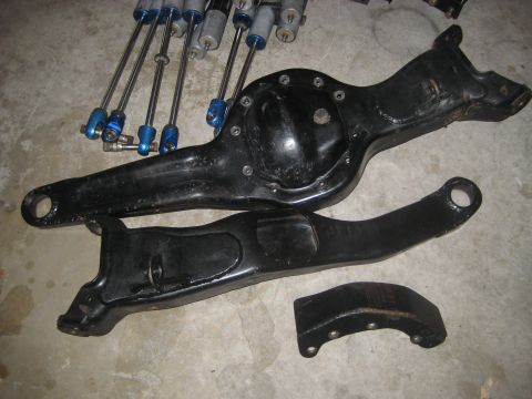 1996 Ford Bronco - Several black metal suspension components and a set of blue and silver shocks are laid out on a concrete surface.