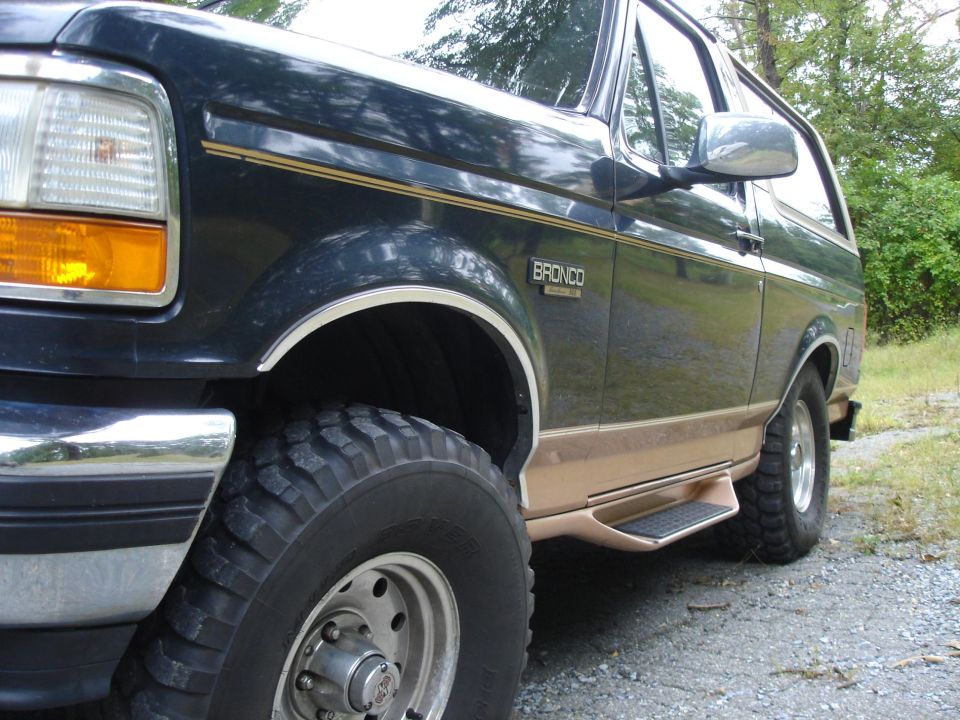 Dark blue Ford Bronco with tan lower trim and running boards, front wheel and fender visible