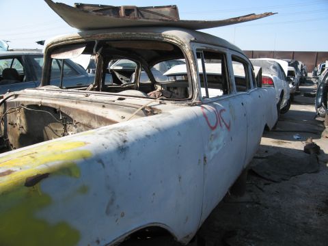 1986 Ford Bronco - Junkyard scene with a stripped 1955 Chevrolet sedan body in the foreground and other vehicles in the background.