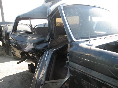 1986 Ford Bronco - This heavily damaged SUV, likely from the 1980s, sits in a junkyard with other vehicles.