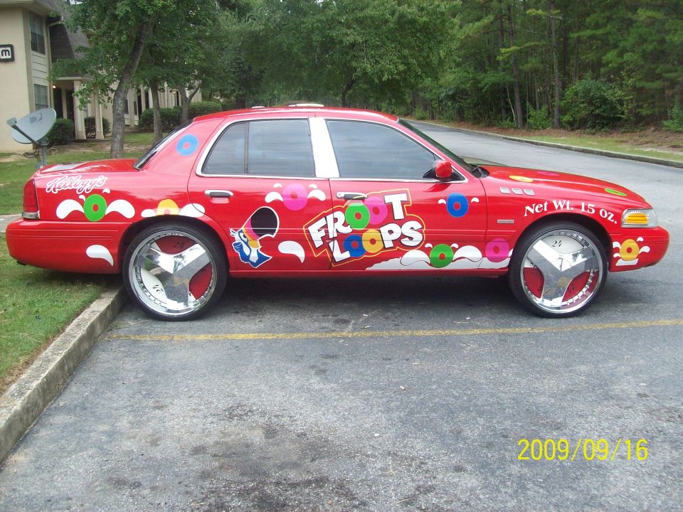 Red sedan wrapped in Froot Loops Kellogg's graphics on large chrome wheels in parking lot