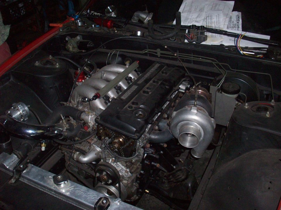 Engine bay with turbocharger, intercooler piping, and intake. Red car exterior visible