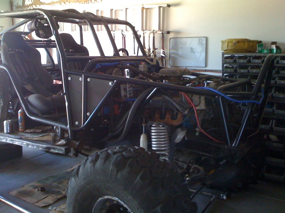 Custom off-road buggy frame with seats and engine exposed, in a garage