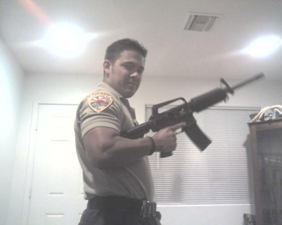 Man in sheriff's uniform holding an assault rifle, indoors