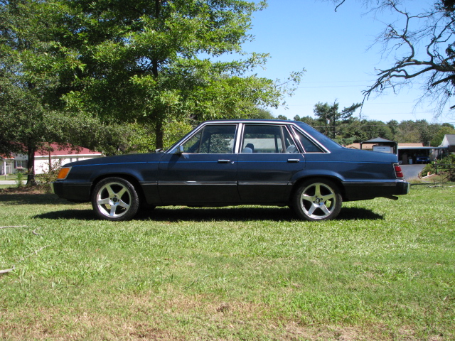 Dark blue four-door sedan with five-spoke alloy wheels, side view on grass lawn