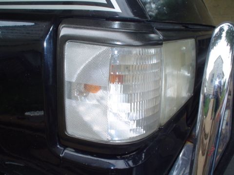 1988 Ford Bronco - Close-up of the front corner of a black SUV, showing the headlight assembly and a portion of a chrome bumper.