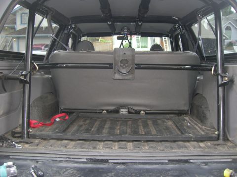 1996 Ford Bronco - The rear cargo area of an SUV shows a roll cage, folded rear seat, and a skull emblem mounted to the back of the seat.