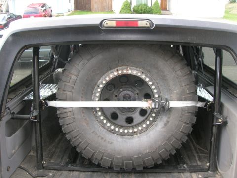 1996 Ford Bronco - Spare tire mount with a large off-road tire secured by a strap within a vehicle's cargo area.