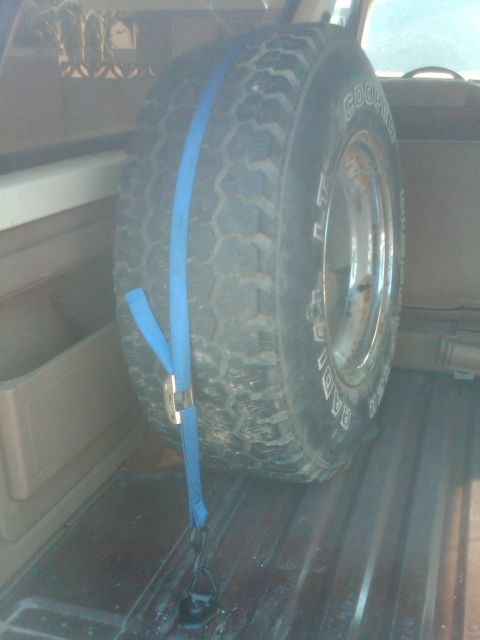 1982 Ford Bronco - Spare tire is strapped down in the cargo area of a vehicle.