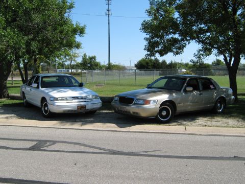 2000 Mercury Grand Marquis - Two sedans, a gold 2000 Mercury Grand Marquis and a white sedan, are parked outdoors on a sunny day.