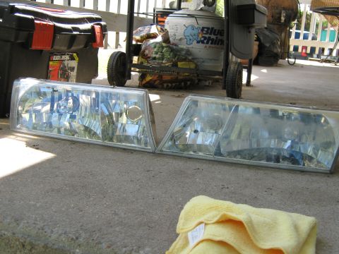2000 Mercury Grand Marquis - Pair of car headlights, possibly from a 2000 Mercury Grand Marquis, resting on a concrete surface.