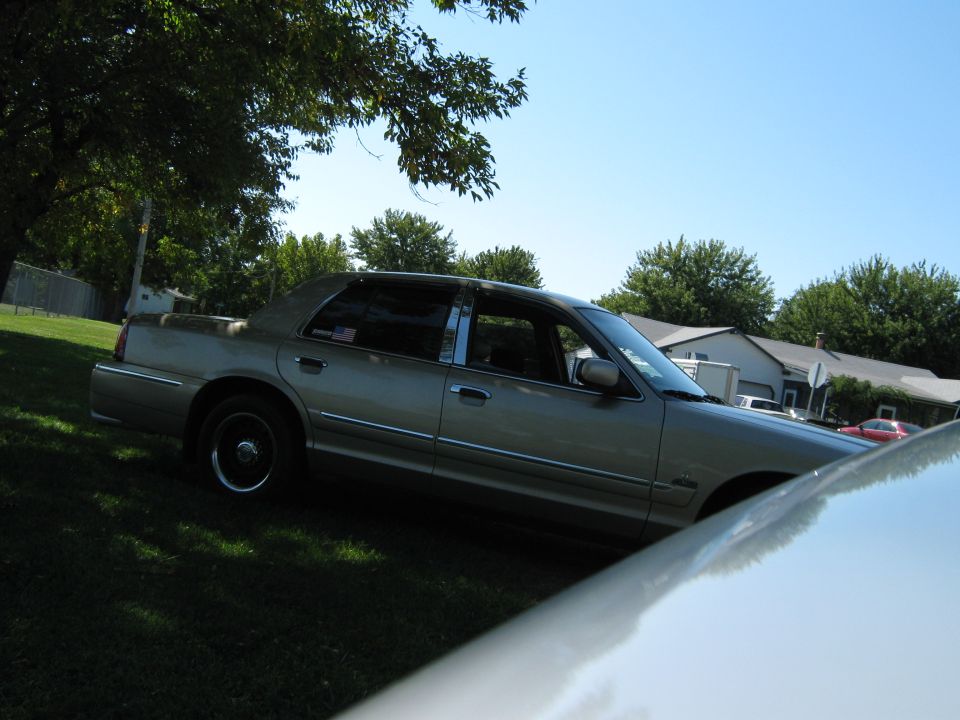 tan 2000 Mercury Grand Marquis parked on a sunny day with trees and houses in the background