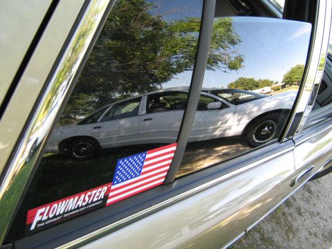 2000 Mercury Grand Marquis - Reflection of a white 2000 Mercury Grand Marquis sedan shows its side profile with trees and sky in the background.