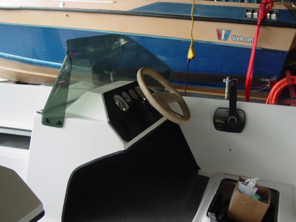 Boat interior with dashboard, steering wheel, and throttle control. A Wellcraft boat is visible in the background