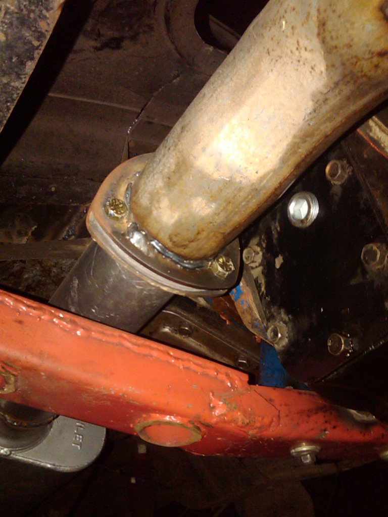 Exhaust pipe flange bolted to a black bracket, with an orange suspension component below