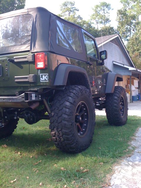 1991 Ford Bronco - Rear view of a lifted green Jeep Wrangler a soft top and prominent off-road tires. The vehicle has a 'JK' badge on the rear quarter panel.