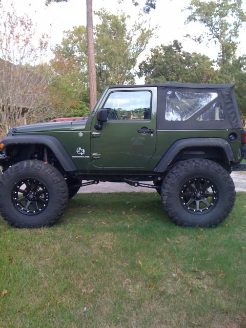 1991 Ford Bronco - Side view of a modified green Jeep Wrangler with oversized tires and black rims.