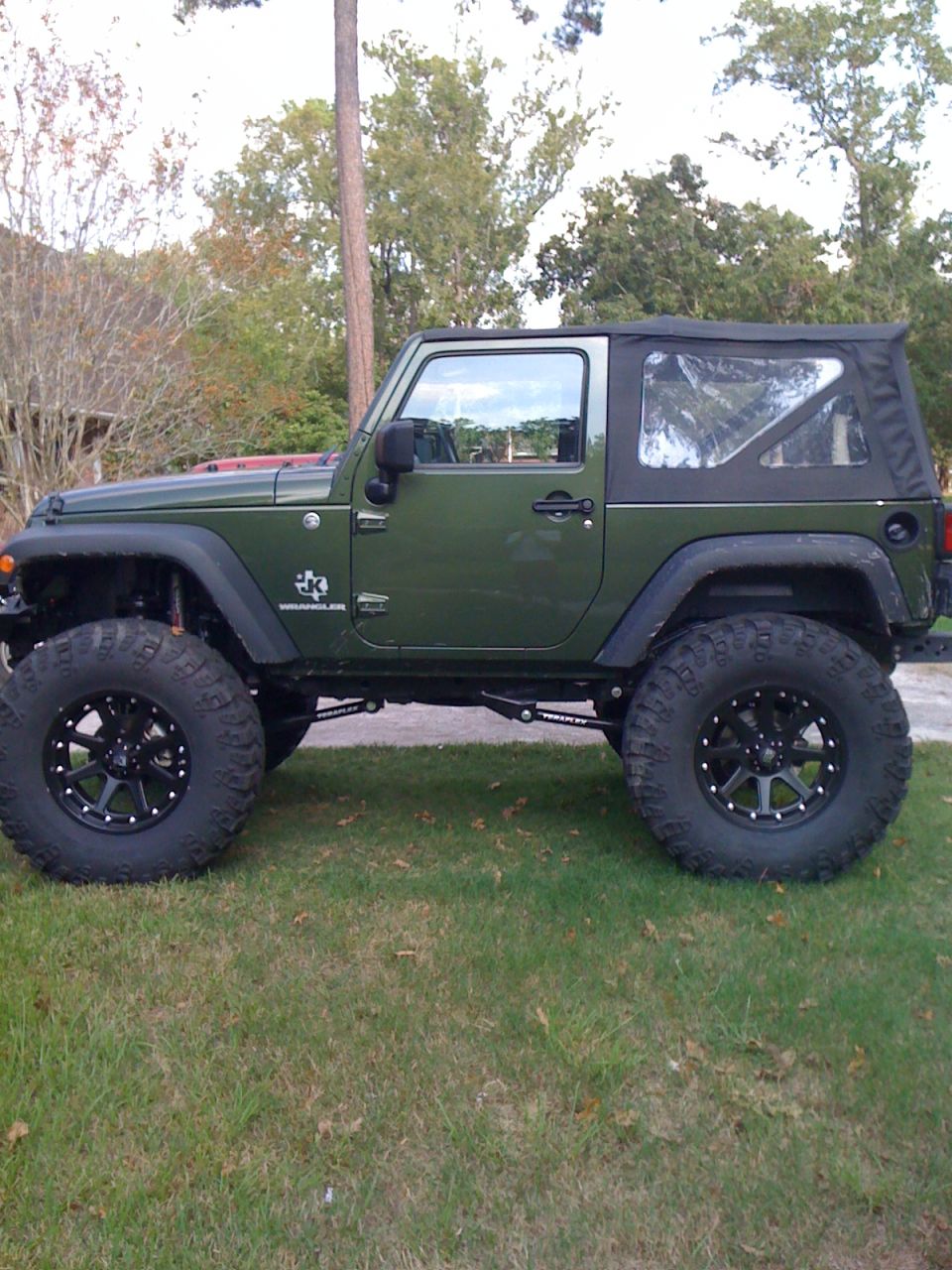 Green Jeep Wrangler with aftermarket wheels and large tires parked on grass
