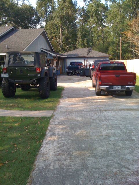 1991 Ford Bronco - A green Jeep Wrangler and a red GMC pickup truck are parked in a driveway next to a house and garage.