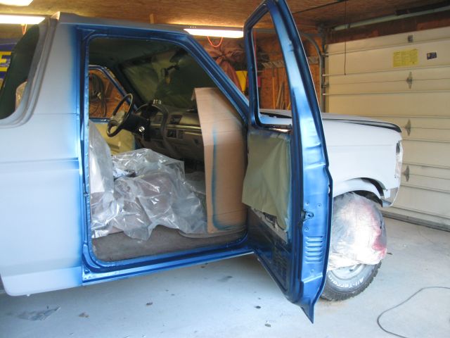 Blue-and-white Ford truck cab interior being prepped with open door in a garage