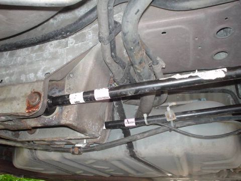 1999 Ford Taurus - Close-up of the underbody showing suspension components and the fuel tank, with some part numbers visible on the bars.