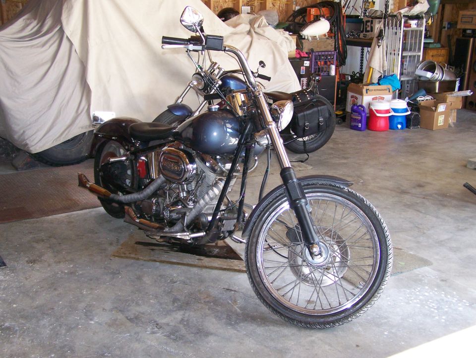 Blue motorcycle front view in garage with another vehicle covered