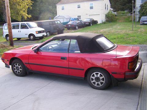1988 Suzuki Samurai - A red convertible is parked in a driveway with other vehicles and houses visible in the background.