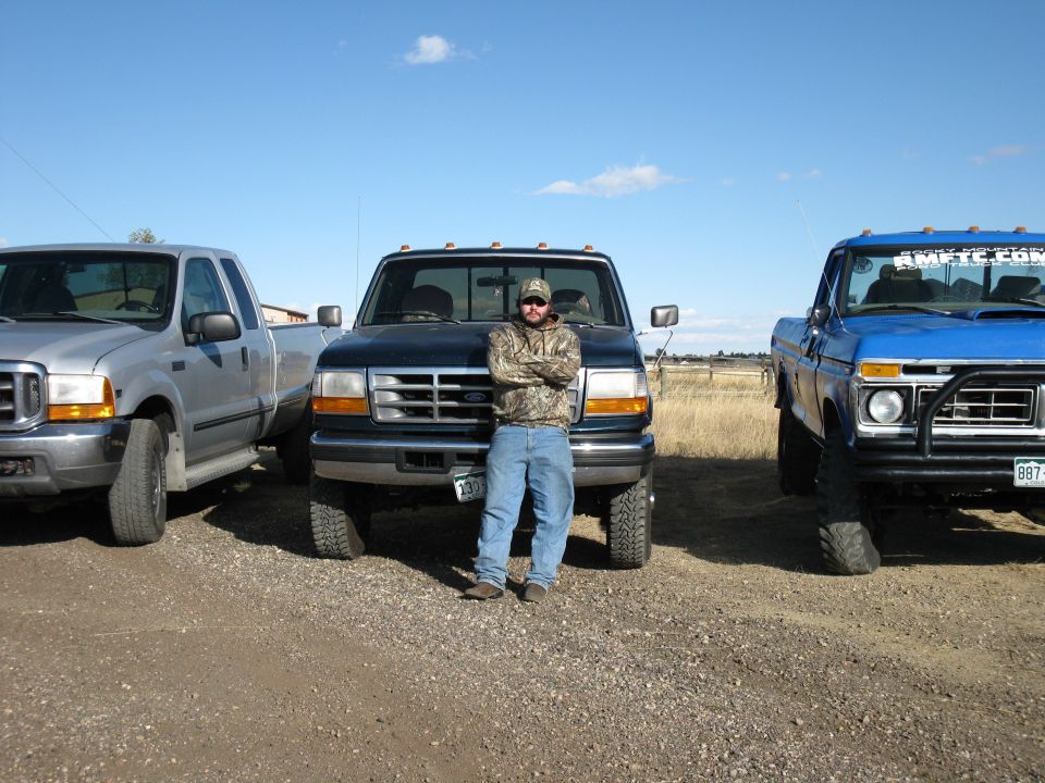 Dark blue Ford F-250 truck from the 1990s, front view, parked between two other trucks