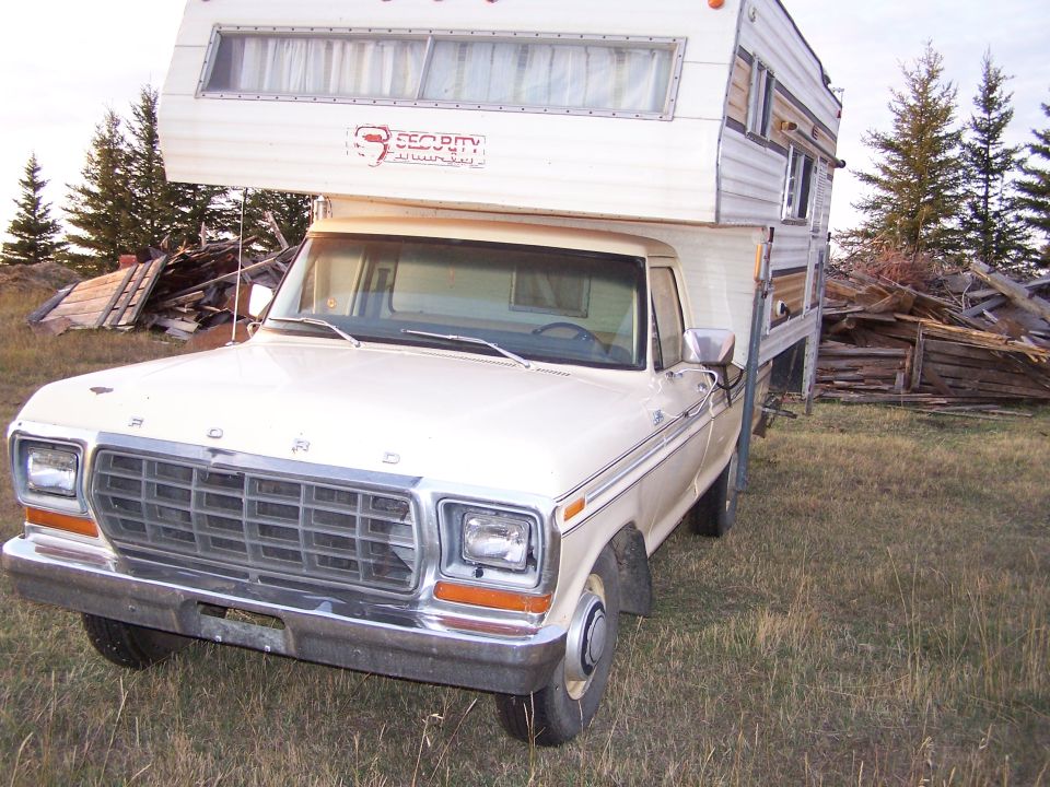 1979 Ford F-250 pickup truck with a camper shell parked in a grassy area with debris in the background