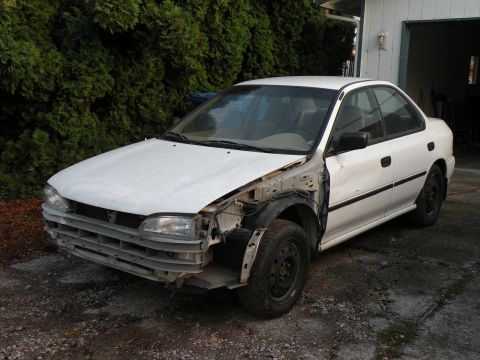1998 Subaru Legacy - A white sedan sits in a driveway with significant damage to its front end.