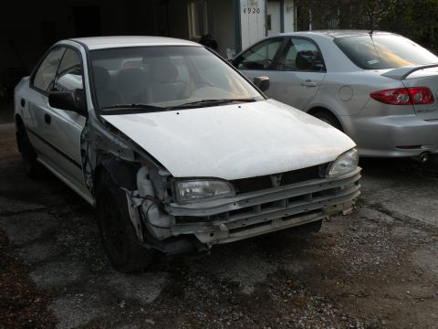 1998 Subaru Legacy - A silver sedan is parked outside, showing damage to its front left side. Another vehicle is visible behind it.