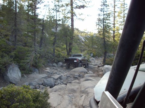 1982 Toyota 4Runner - Two off-road vehicles navigate a challenging, boulder-strewn path through a wooded mountainside.