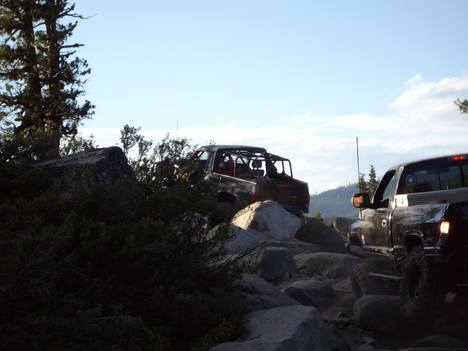 Two off-road vehicles navigate a rocky trail under a clear sky