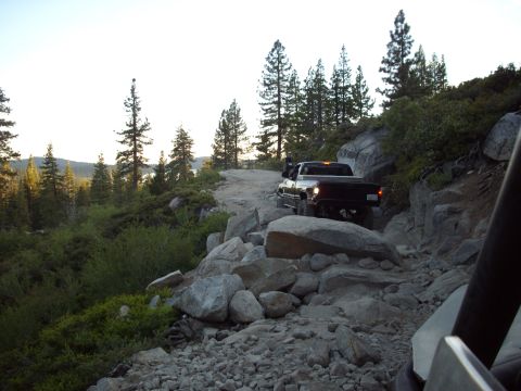 1982 Toyota 4Runner - A pickup truck drives over a challenging, boulder-strewn path in a mountainous, wooded area.