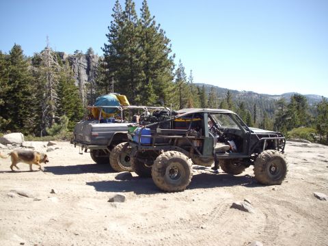 1982 Toyota 4Runner - Two custom off-road vehicles are parked on a rocky, dirt terrain with a dog nearby.