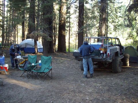 1982 Toyota 4Runner - A heavily modified SUV with oversized tires is parked at a campsite in a forest, with people setting up camp.
