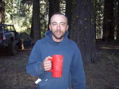 1982 Toyota 4Runner - A man poses for a photo while holding a red mug in a wooded area, with camping gear visible.