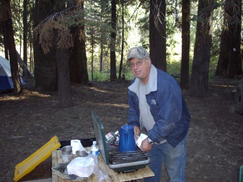 1982 Toyota 4Runner - A man prepares food at a campsite, with tents visible among the trees.