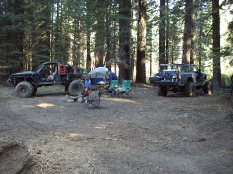 1982 Toyota 4Runner - Two heavily modified off-road vehicles are parked at a campsite in a wooded area.