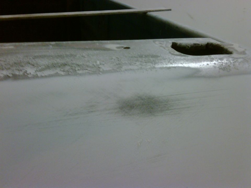 Close-up of a vehicle's body panel, possibly undergoing repair or preparation for paint. Shows some sanding marks and a dark smudge