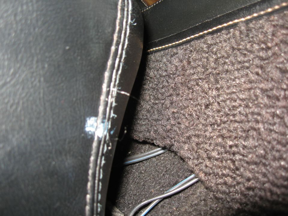Close-up of car's center console area showing black leather trim and dark carpet with some wires visible
