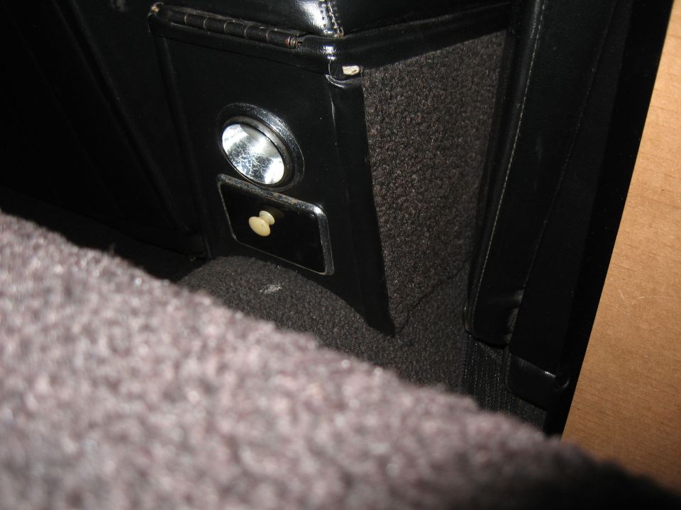Black car interior console with chrome-trimmed ashtray and lighter, showing carpeted floor