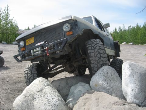 1990 Ford F-250 - This heavily modified Ford F-Series truck is shown off-road, tackling a rocky terrain with its aggressive tires and winch.