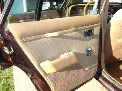 1984 Ford LTD - The interior door panel of a car features tan fabric and vinyl trim with chrome accents.