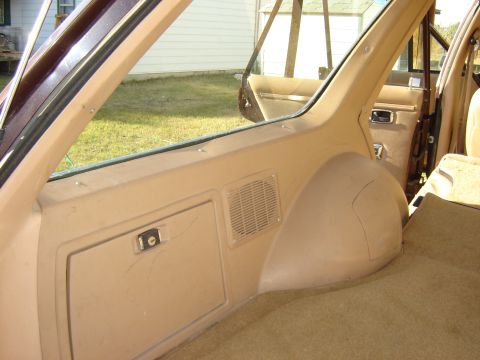 1984 Ford LTD - The rear interior of a station wagon features tan carpeting and trim panels with a visible storage compartment and speaker grille.