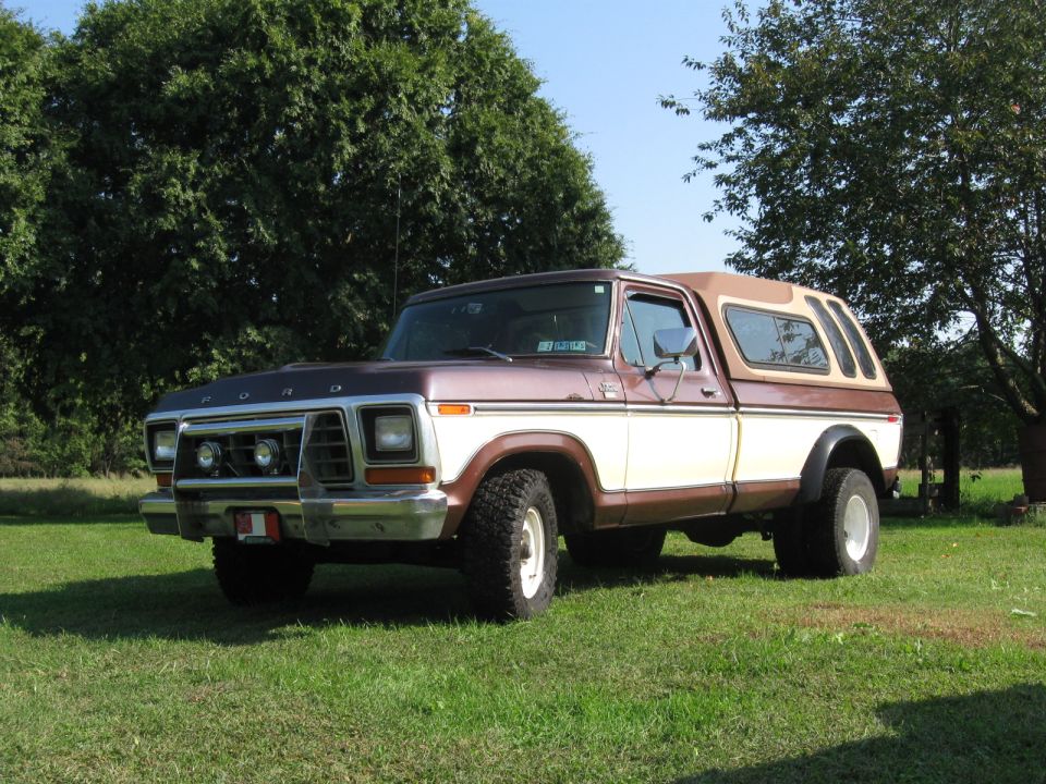 Brown and tan late-1970s Ford pickup with camper shell parked on grass