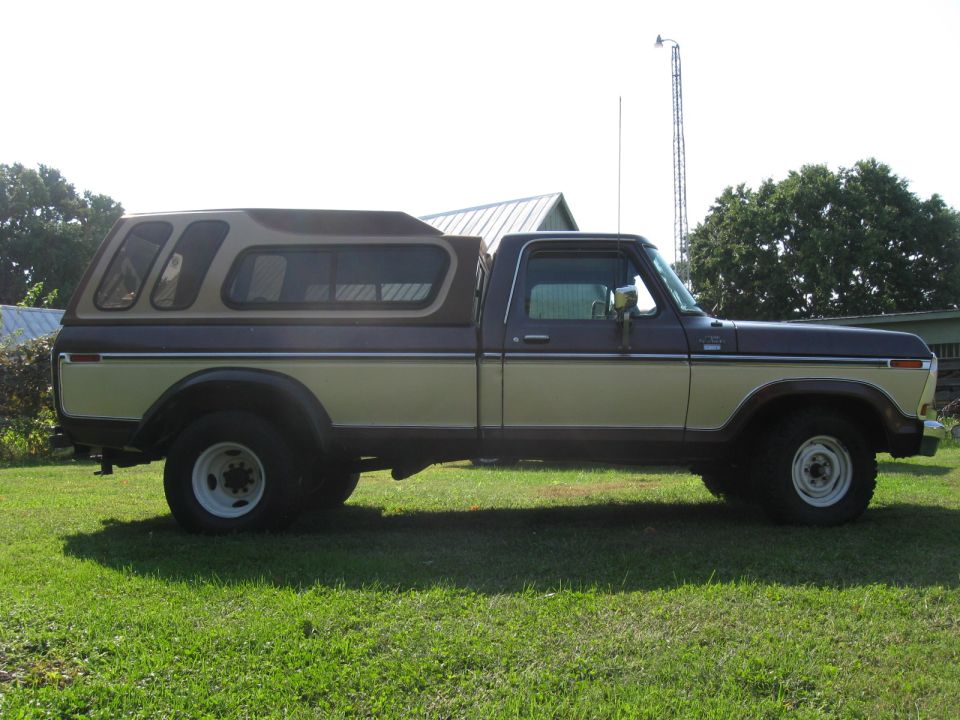 Side profile of brown and tan Ford pickup with camper shell on grass