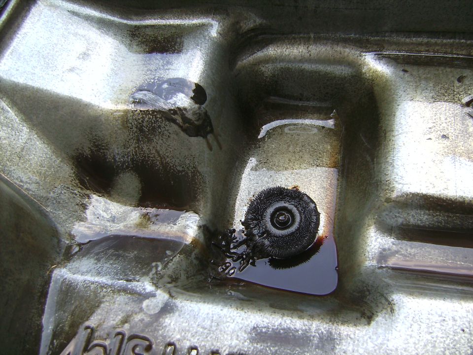Magnetic drain plug covered in metal filings inside an oily metal pan
