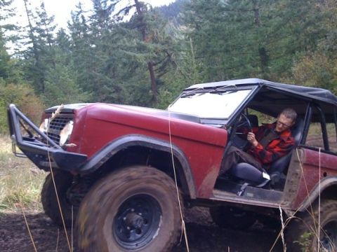 1968 Ford Bronco - A man drives a red 1968 Ford Bronco through a muddy, wooded area.