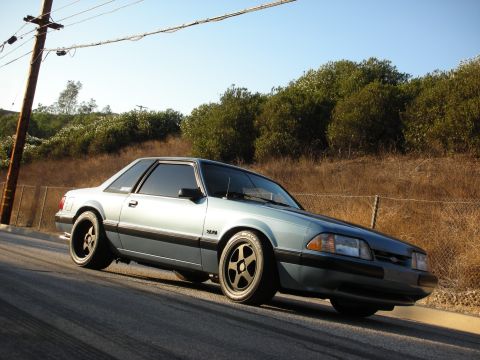 1990 Ford Mustang - A light blue 1990 Ford Mustang coupe is seen from a 3/4 front angle, black trim and aftermarket wheels.